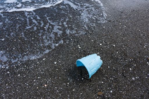 A blue plastic toy bucket partially buried in the sand