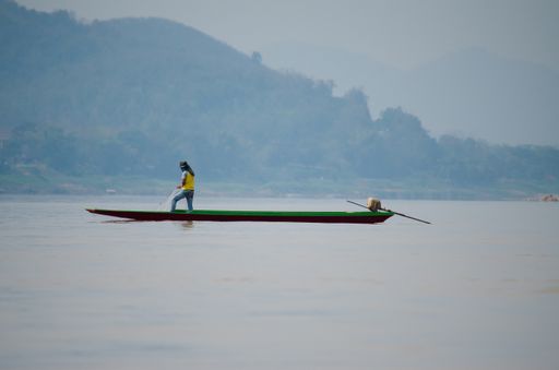 A person standing on the sea kayak on the water with mountains in the background