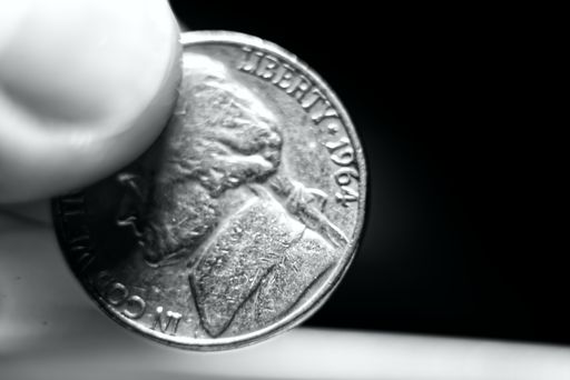 A selective focus grayscale shot of a person holding a coin with his fingers