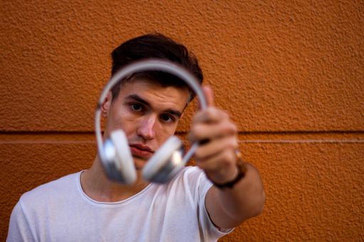A beautiful shot of young Caucasian guy DJ showing his headphones to the camera on orange background