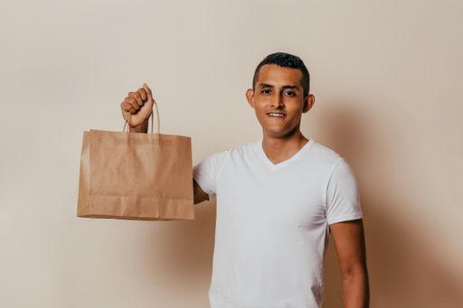 A closeup shot of a young Latinx man with a white t-shirt holding a recyclable paper bag