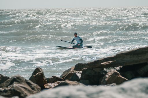 An Argentinian male riding a paddleboard with rocky coast foreground
