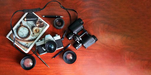 A top view of travel concept with a retro camera, lens, map, compass, and pens on a wooden table