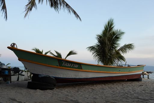A boat on a tropical beach with palm trees in background in Pattaya, Thailand