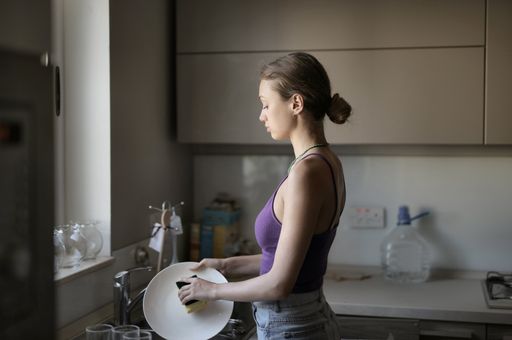 A young female washing the dishes in the kitchen under the lights