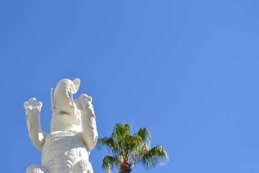 A low angle shot of a white elephant statue near a palm tree under a clear blue sky