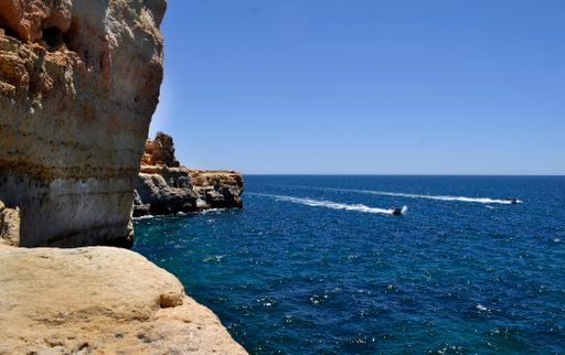 The boats on the sea water near rock formations against a clear blue sky on a sunny day