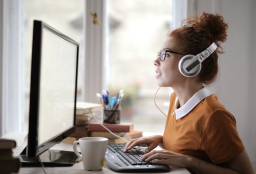 A young woman with headphones and glasses working on the computer under the lights in a house