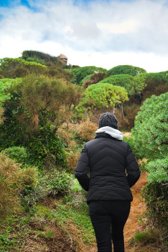 A vertical back view of a Caucasian woman standing in a field with bushes in Italy