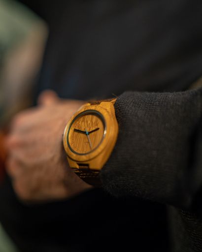 A vertical selective closeup shot of a person wearing a black suit with a yellow watch in his wrist