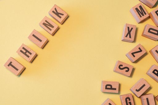 The word THINK taken from a pile of wooden letter blocks with yellow background and copy space