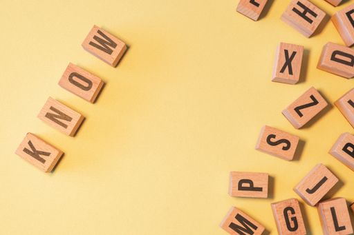The word KNOW, taken from a pile of wooden letter blocks with yellow background and copy space