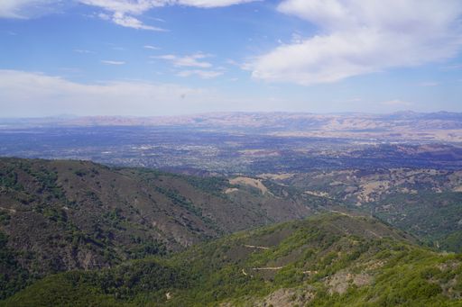 A beautiful view of mountains covered by trees and small bushes under the blue sky with clouds