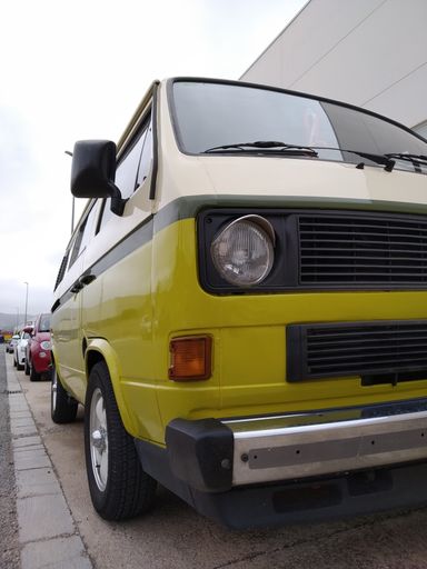 A vertical shot of a vintage camper van in olive green, cream white, and dark green parked at the street