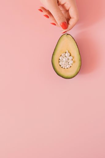 A woman's hand holding an avocado with pearls rather the seeds on a white surface