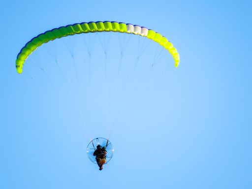 A low angle shot of a person in powered paragliding under a clear blue sky