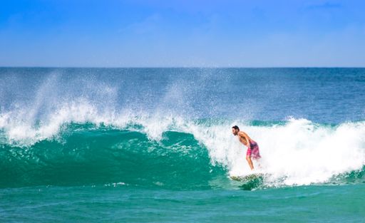 A man surfing on big waves on the island of Santa Catarina at Mole beach under a blue sky on a sunny day