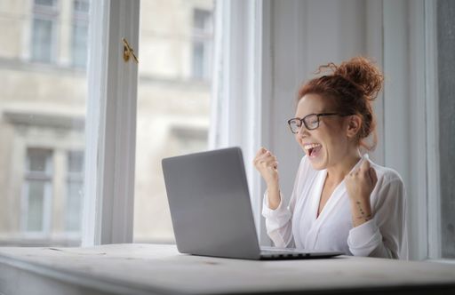A cheerful woman with glasses sitting in front of the laptop on the table under the lights in a house
