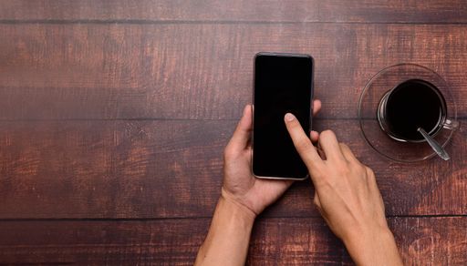 A Top view of a Coffee cup, a hand holding and using a smartphone