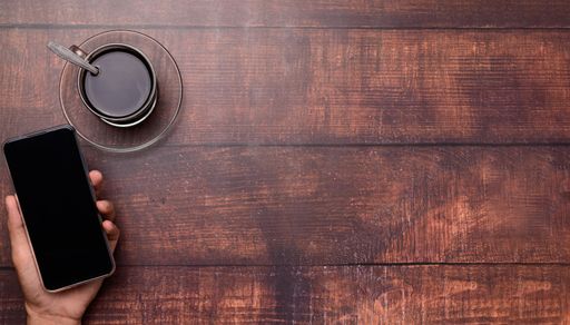A Top view of a Coffee cup, a hand holding and using a smartphone