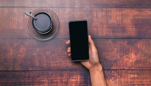 A top view of a Coffee cup, a hand holding and using a smartphone