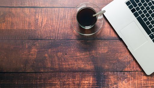 A Top view of a coffee mug, notebook, and laptop on a wooden surface in a working atmosphere