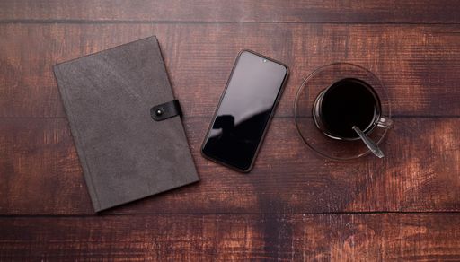 A Top view of a coffee mug, notebook, and smartphone on a wooden surface in a working atmosphere