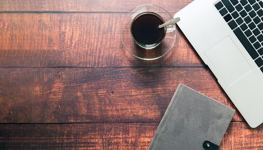 A top view of a coffee mug, notebook, and laptop on a wooden surface in a working atmosphere