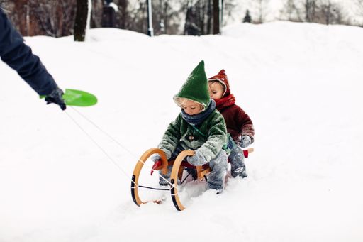 A hand pulling a sled with two cute Caucasian kids in a snowy winter field