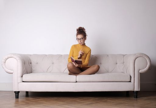 A thoughtful female sitting on the couch and holding a pencil with a book under the lights
