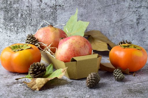 Autumn composition with pomegranates in a wooden box, leaves, persimmon fruits, and cones in the grunge background