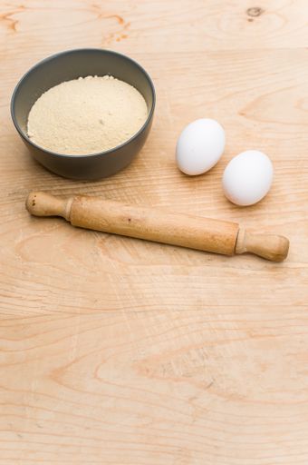 rolling pin white eggs and dark gray bowl with wholegrain flour on worn wooden background with copy space