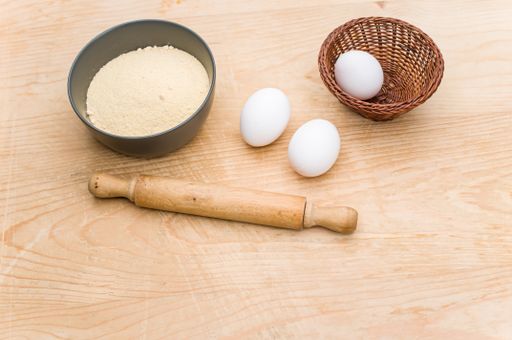 white eggs and dark gray bowl with whole grain flour and rolling pin on worn wooden background with copy space