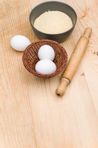 white eggs and dark gray bowl with whole grain flour and rolling pin on worn wooden background with copy space