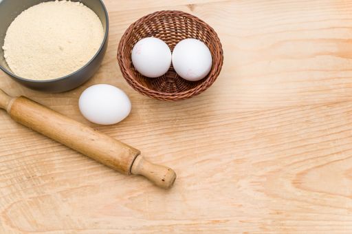 white eggs and dark gray bowl with whole grain flour and rolling pin on worn wooden background with copy space