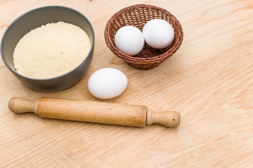 white eggs and dark gray bowl with whole grain flour and rolling pin on worn wooden background with copy space