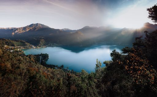Scenic view of a tranquil lake surrounded by mountains under a clear sky, with sunlight streaming over the landscape.