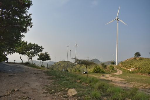 Selective focus photo of Multiple Windmills which are source of renewable energy functioning on top of hill on a sunny day against a blue sky in India