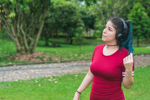 A Hispanic student listening to music with her wireless headphones in a park
