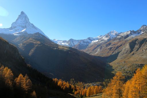 Golden autumn landscape with the Matterhorn above Zermatt, Switzerland. Snowy peaks, blue sky, and colorful larch trees.