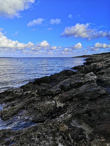 a vertical shot of a beautiful calm beach with a rocky hill in Malta captured on a sunny day