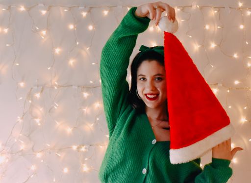 A shot of a Caucasian girl holding Santa hat and smiling with Christmas lights on the wall
