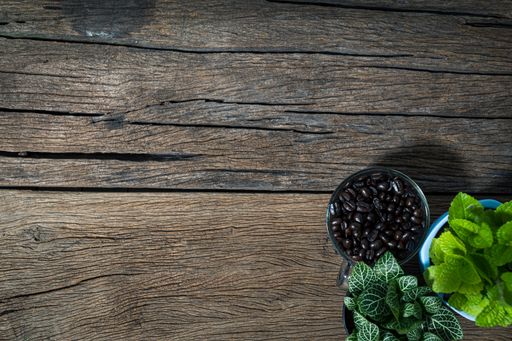 A top view of a wooden table with a bowl of coffee beans, potted plants, and copy space