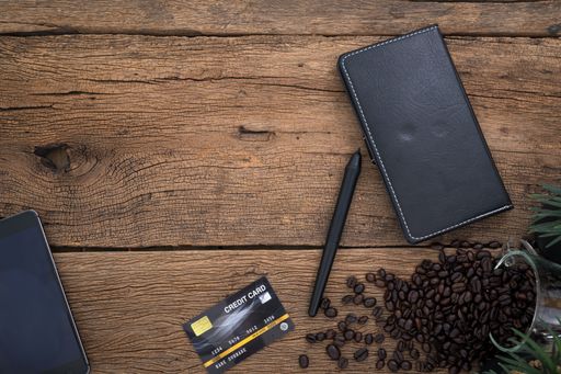 A top view of a wooden table with a notebook, a pen, a credit card, and coffee beans