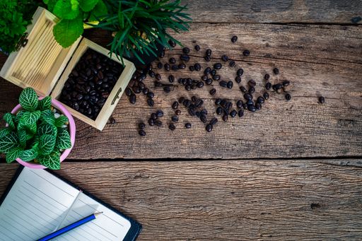 A top view of a wooden table with coffee beans, a potted plant, a notebook, and copy space