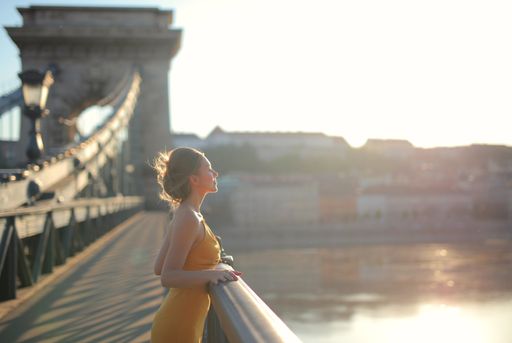 A young female in a yellow dress standing on the Szechenyi Chain Bridge under the sunlight in Hungary