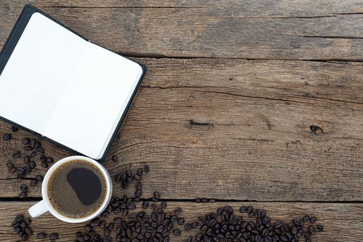 A top view of a cup of coffee with coffee beans and a notebook on a wooden table