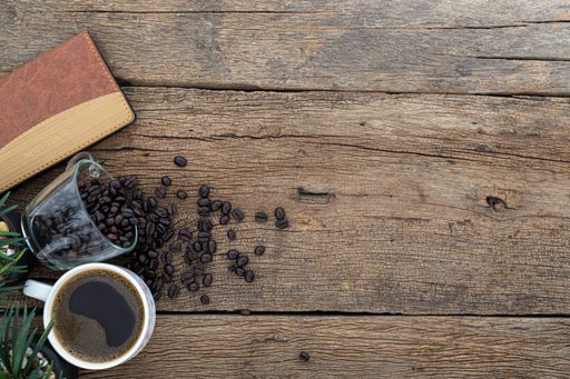 A top view of a cup of coffee with coffee beans and a notebook on a wooden table