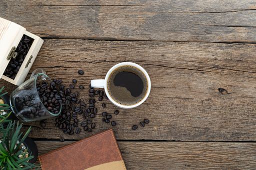 A top view of a cup of coffee with coffee beans and a notebook on a wooden table