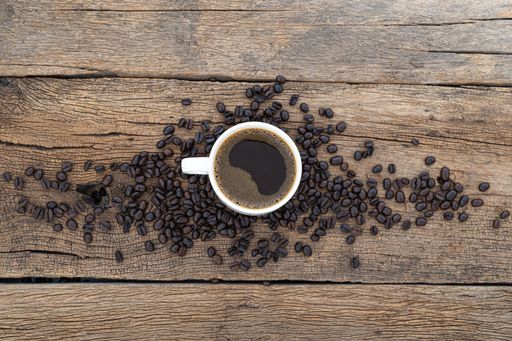 A top view of a cup of coffee with coffee beans on a wooden table